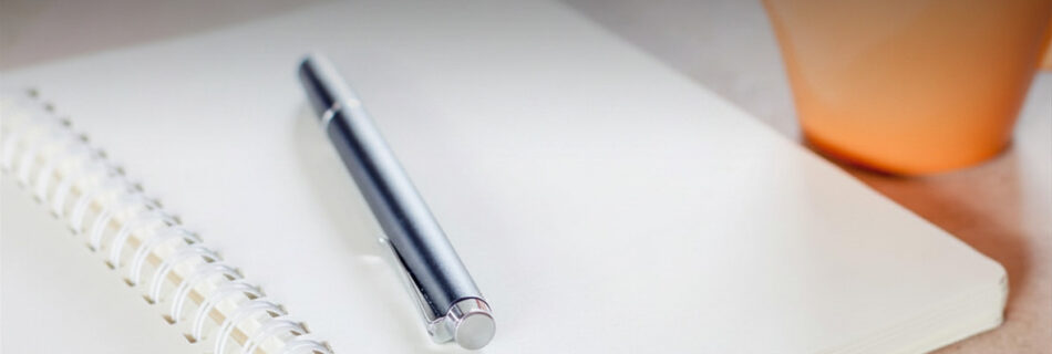 An open notebook with a pen resting on a blank page beside a coffee cup, suggesting the pause before a considered decision.