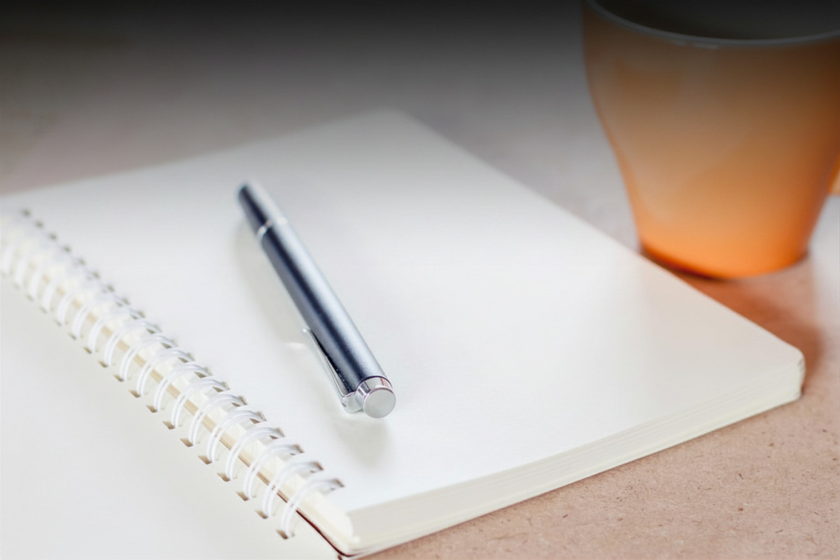 An open notebook with a pen resting on a blank page beside a coffee cup, suggesting the pause before a considered decision.