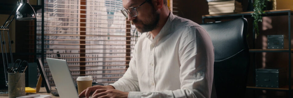 An engineering professional working at a laptop with a drawing set set aside, illustrating the business capabilities required for AEC practice leadership.